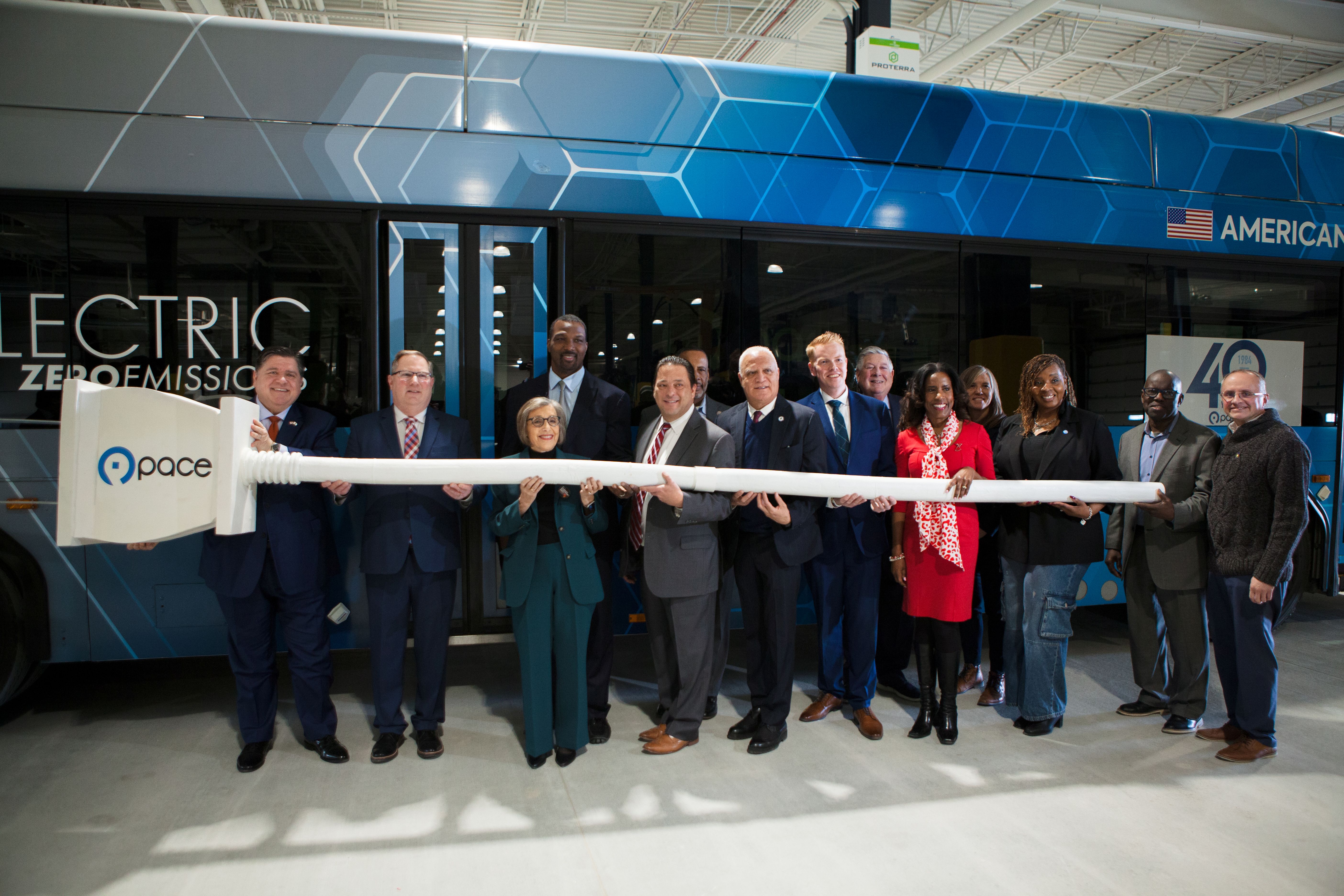 Photo of elected officials and Pace leaders posing in front of electric bus with oversized electrical plug