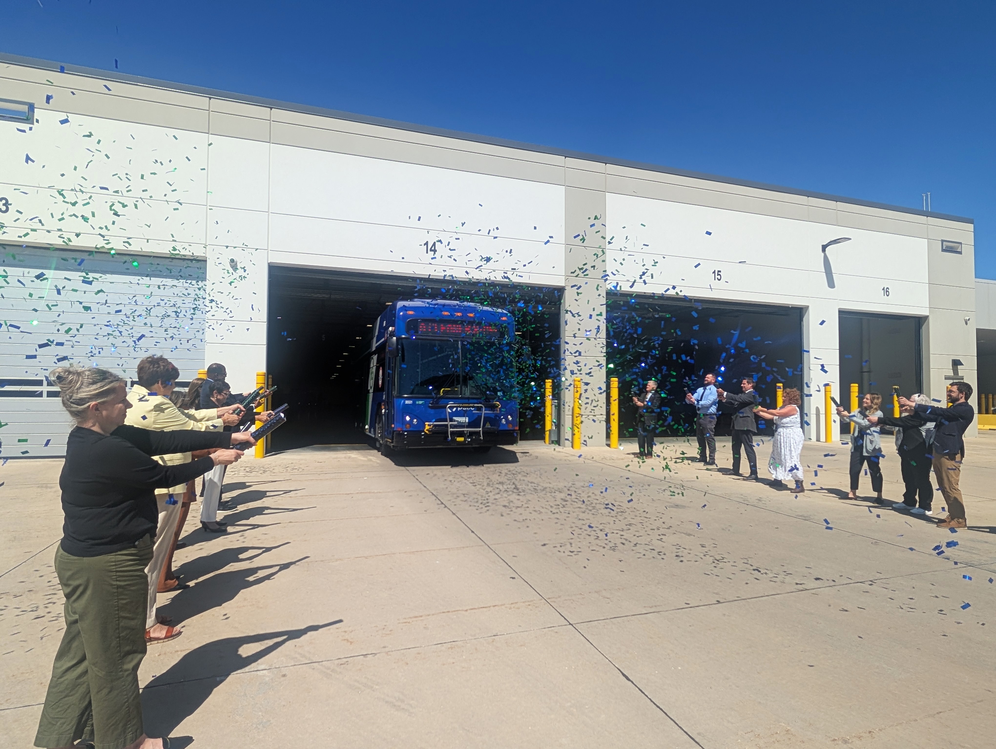Photo of Pace staff and local officials opening firecracker poppers outside of a garage as a new hybrid-electric bus leaves the garage.