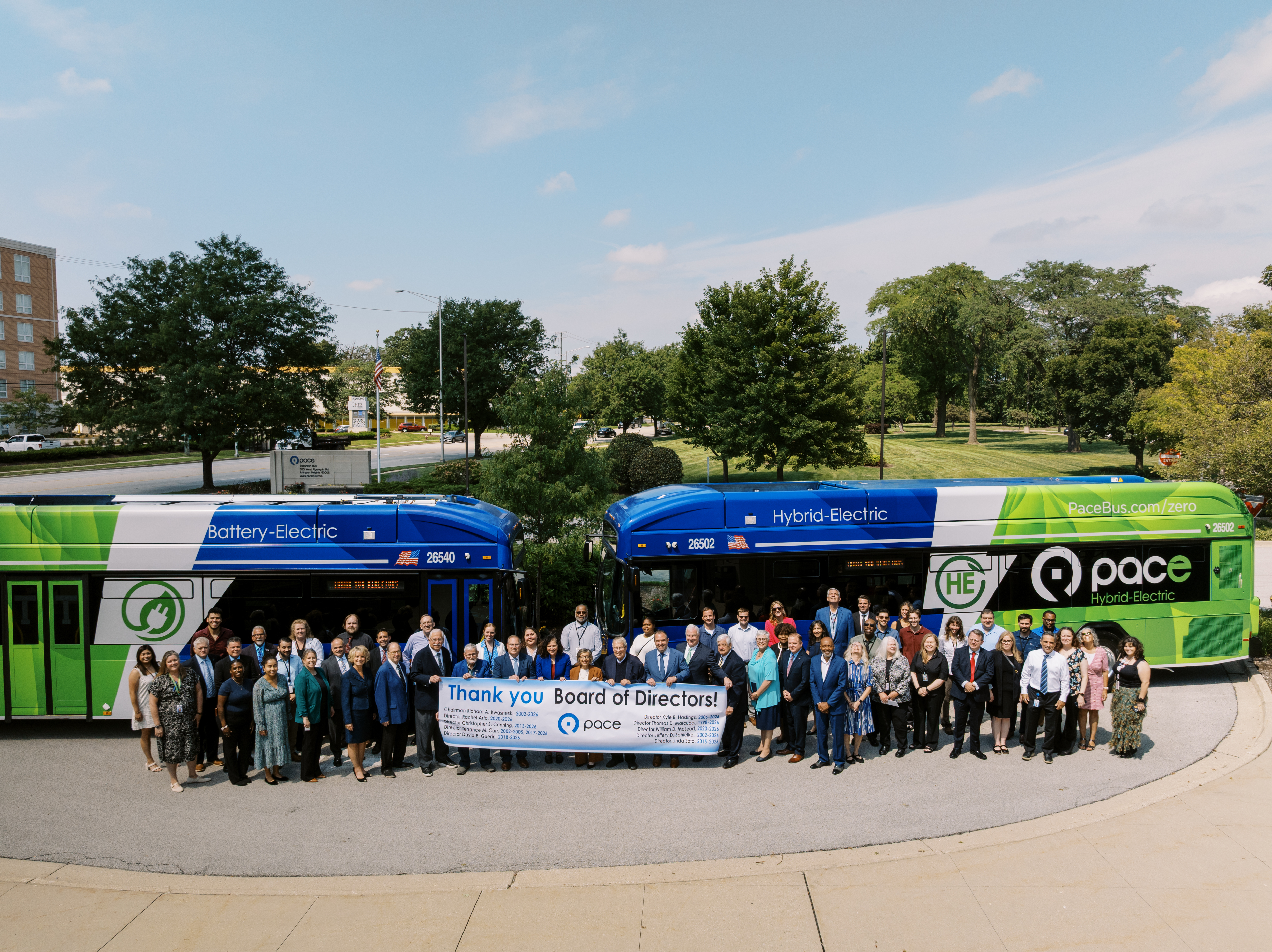 Photo of Pace Board members, leaders, and staff standing in front of two electric buses outside at Pace Headquarters with Pace Board members holding a banner that says, "Thank you to the Pace Board of Directors".