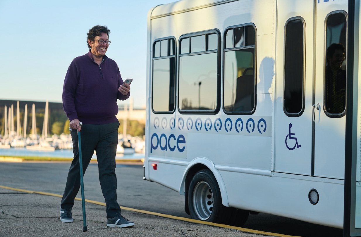 male using walking cane and looking at smartphone outside Pace paratransit bus