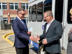 image showing two men in suits are shaking hands in front of a MCRide bus 